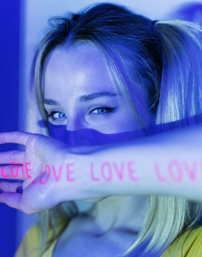 Na zdjęciu widać kobietę, która trzyma rękę przed sobą i zakrywa połowę twarzy. Na dłoni tej kobiety widnieje napis 